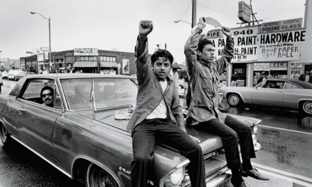 Two young Chicano men ride on the hood of a car and raise their fists during a National Chicano Moratorium Committee march in Los Angeles, California, on August 29, 1970, in opposition to the war in Vietnam.