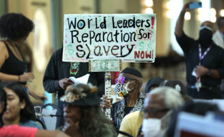 A man holds up a sign that reads "World Leaders, reparations for slavery now!"