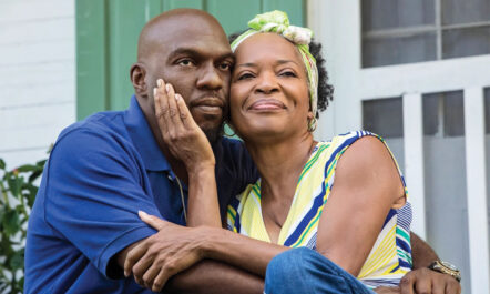 Hollywood Desonier, left, played by Omar J. Dorsey, sits on a porch next to on-screen squeeze Violet Bordelon (“Aunt Vi”), played by Tina Lifford, in Queen Sugar. Aunt Vi's is smiling as her hand cradles Hollywood's face.