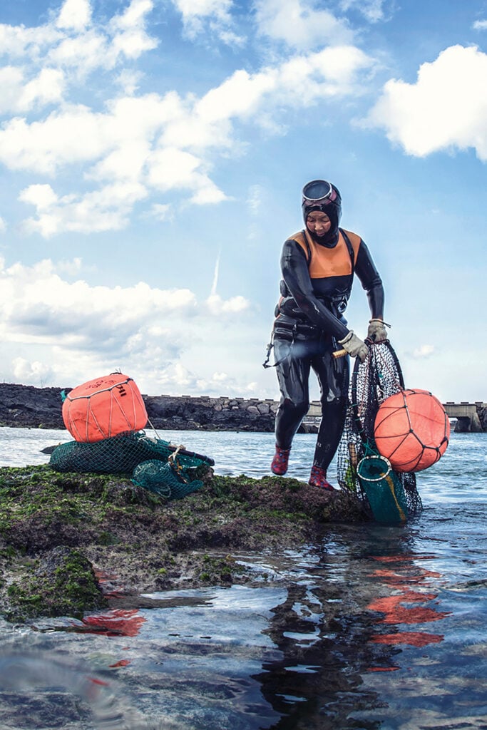 A haenyeo diver, still wearing her wetsuit, goggles, gloves and vest, pulls up her net and flotation device after a dive off the coast of Jeju Island in Korea.