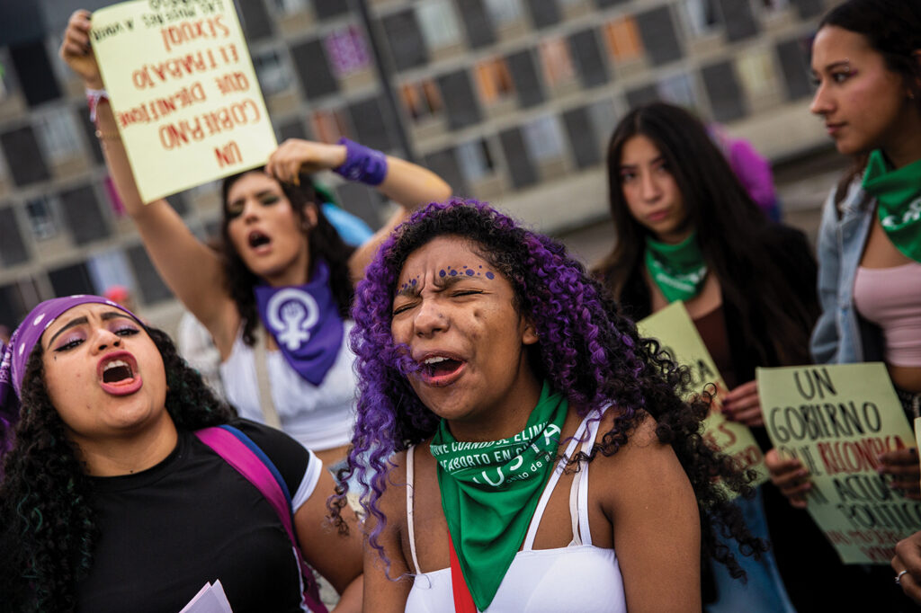 A group of demonstrators, some with purple hair and purple or green bandanas, shout feminist slogans at a march in Bogota, Colombia, on June 11, 2022. 