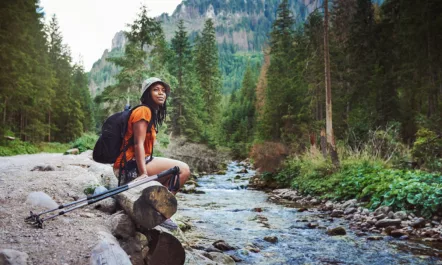 Woman overlooking a rivebank in the outdoors with hiking poles in the outdoors