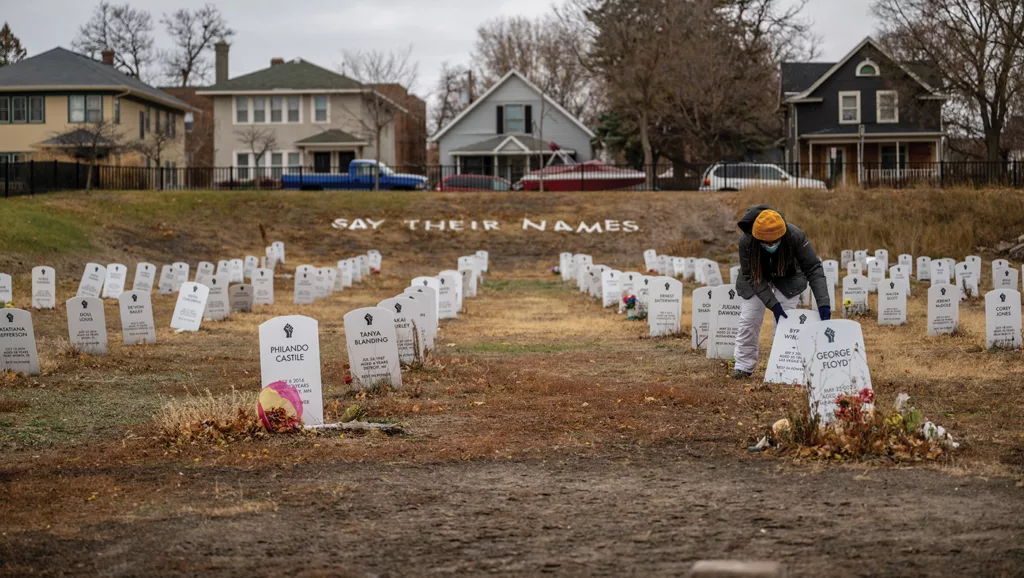 Marcia Howard, a community member and activist in Minneapolis, Minnesota, straightens mock tombstones in November 2022 in the Say Their Names Cemetery, an art installation that sits in a grassy park one block north of the George Floyd Memorial. Names visible on the tombstones include Philando Castile, George Floyd, Tank Blanding, and more. 