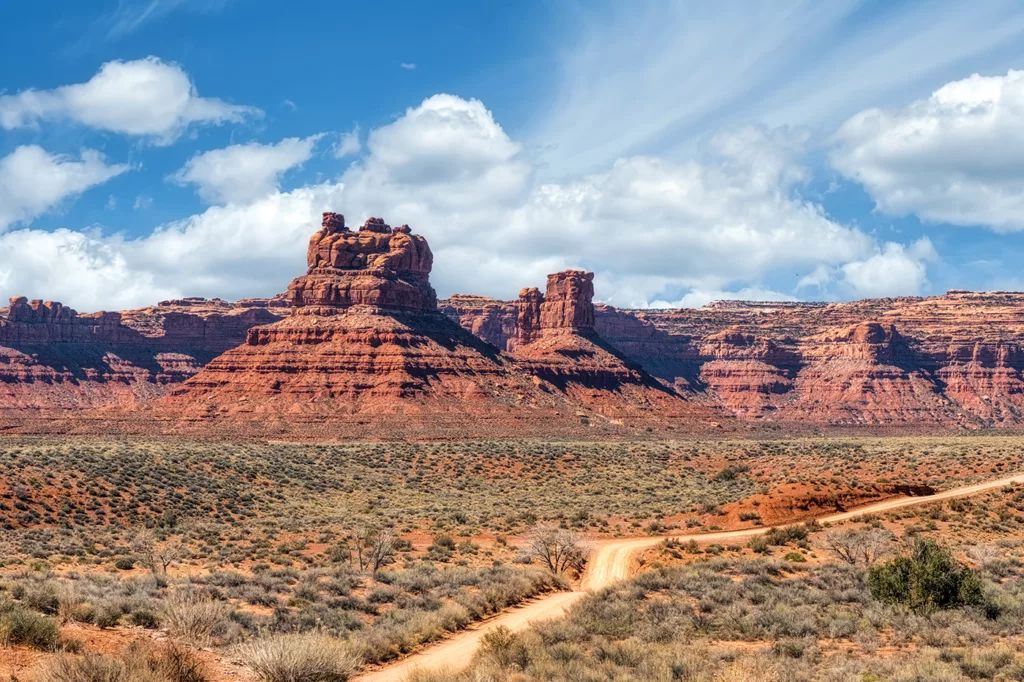 A landscape photo shows red rock formations arising from the arid sand and shrubbery of Bears Ears National Monument in Utah.