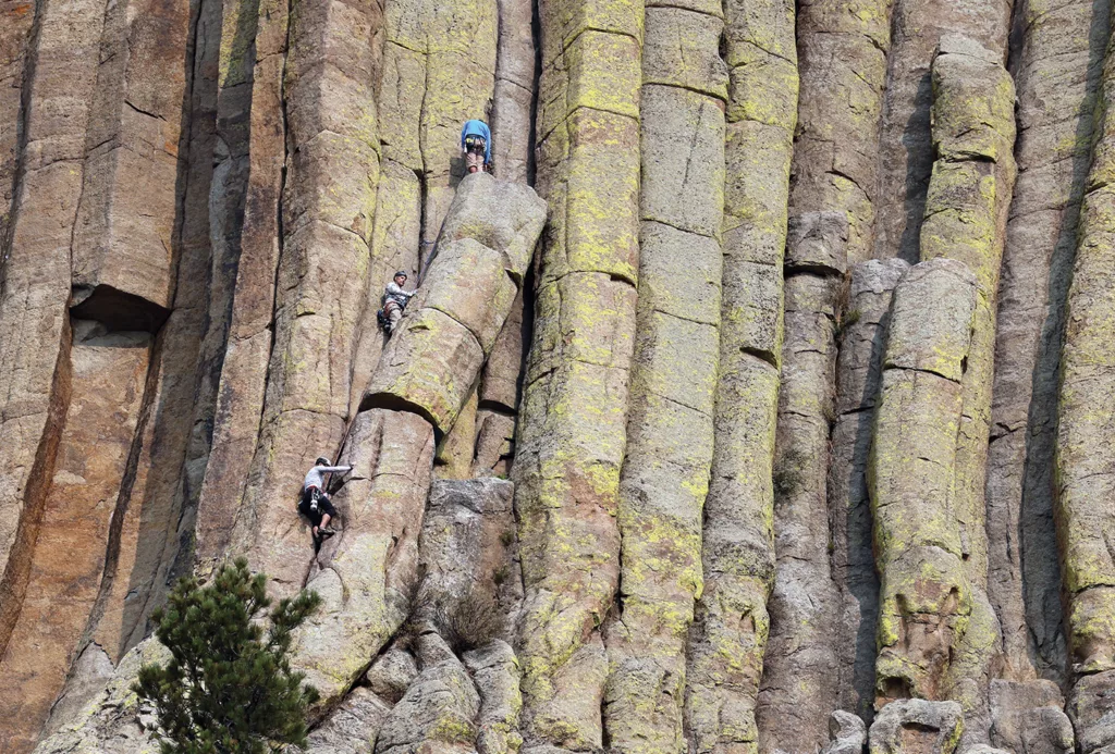 Three rock climbers scale a column of Bear's Lodge, or Devils Tower.