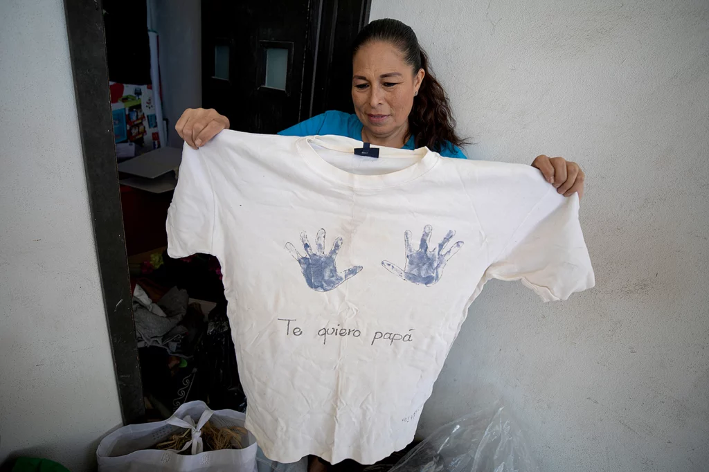 Elva Rivas holds up a white t-shirt with two blue handprints and the words "Te quiero papá" (I love you, dad"), made by her son, Roberto Sebastián, four years before his father, Roberto Maciel, disappeared.