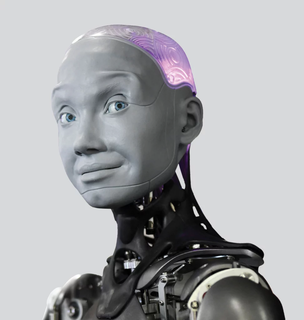 The Engineered Arts Ameca humanoid robot stares at the camera, with a slate-grey humanoid face, blue eyes, and mechanical neck and shoulders.