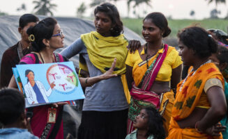 Maya Patil holds open a book depicting the uterus to a group of migrant sugarcane workers in India.