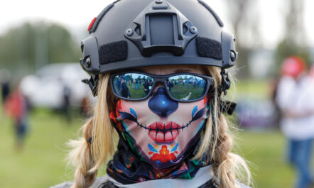 A close-up photo of a white, blonde female protester in Portland, Oregon. She is wearing a protective helmet, sunglasses, and a face mask concealing her mouth and nose.