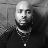 A bald Black man with a beard looks at the camera