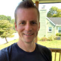 a white man with a brown mohawk smiles at the camera