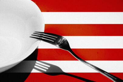 A fork leans on an empty plate, over red stripes of USA flag